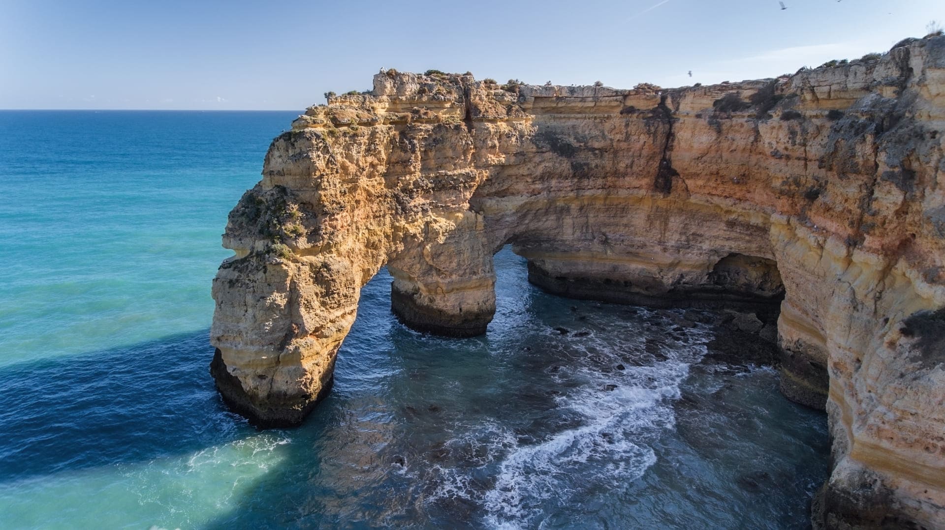 Praia da Marinha com fal&eacute;sias e mar azul.